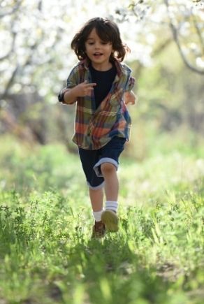 Roześmiane dziecko biegnące w butach po trawie 