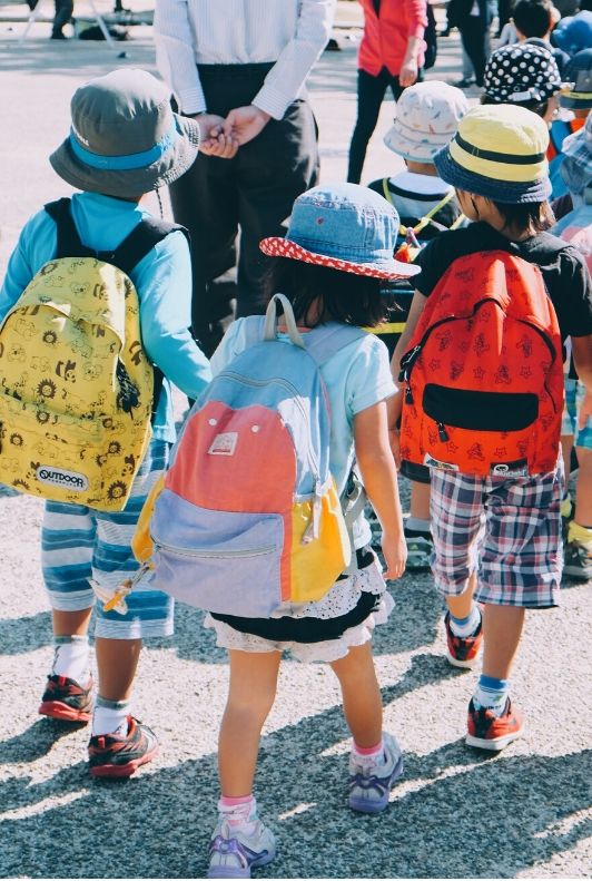Dzieci z plecakami szkolnymi na spacerze z nauczycielką